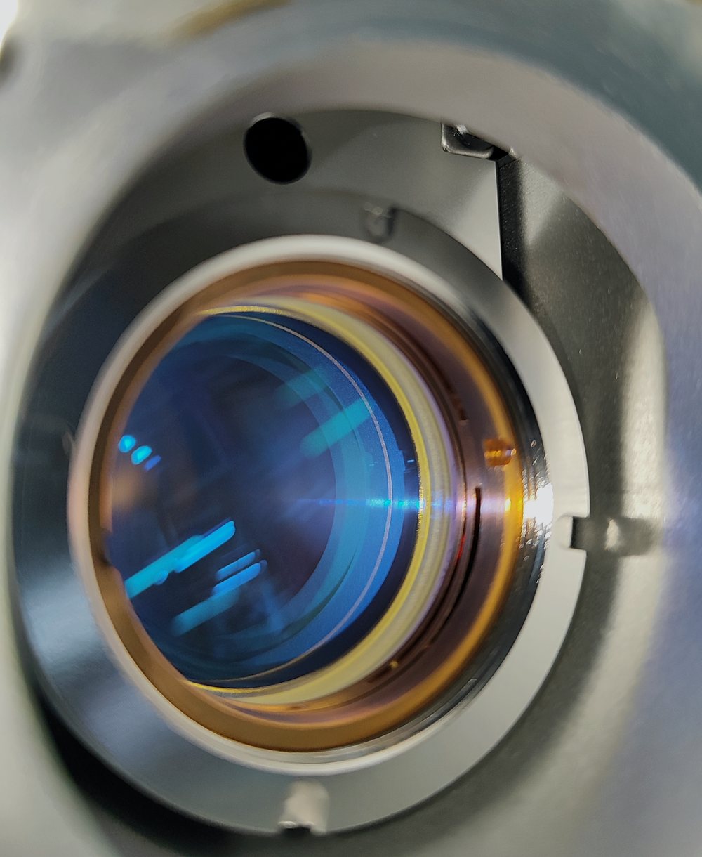 Lente de foco montada no cabeçote, com o tratamento óptico refletindo em azul e dourado